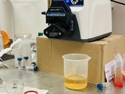 Peristaltic pump dispensing yellow liquid into a clear container on a laboratory bench